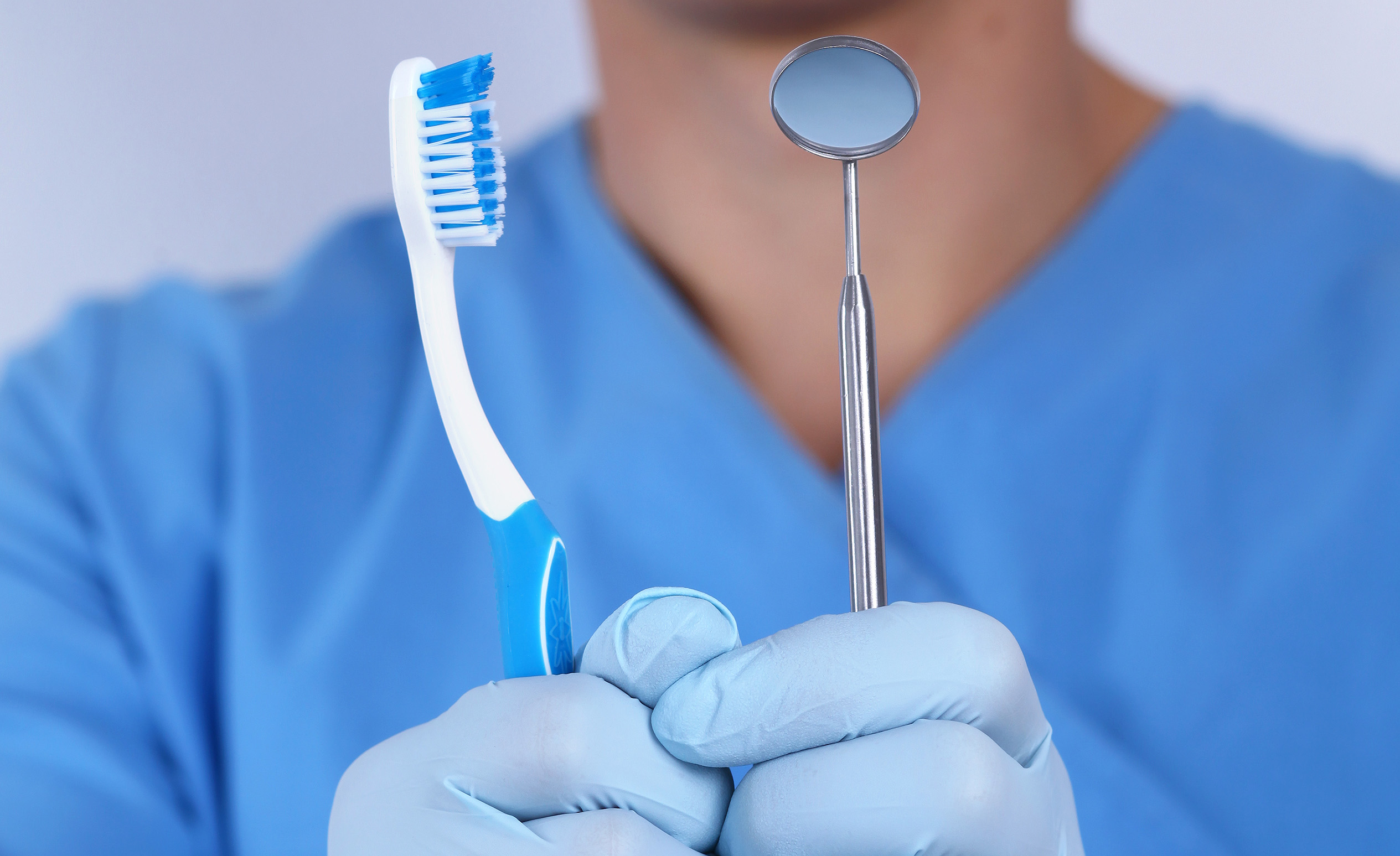 The dentist holding a toothbrush and a dental examination mirror as the means for fighting tooth gum inflammation